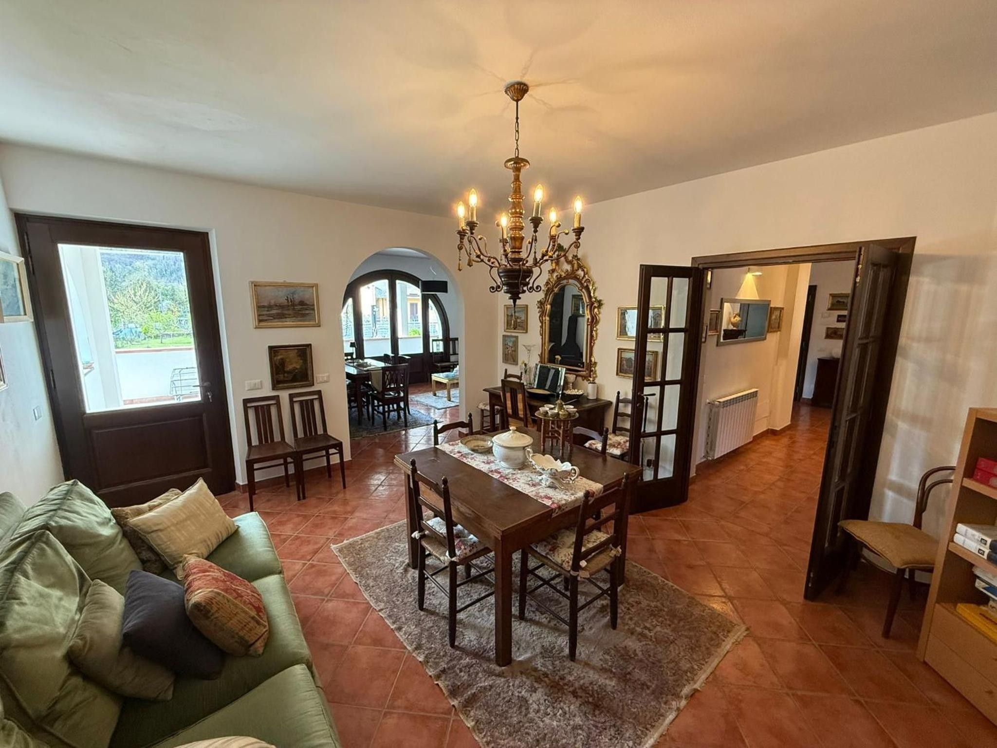 Uma sala de estar ampla com uma mesa de jantar, cadeiras, um sofá verde e um lustre.