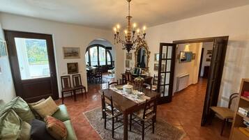 Uma sala de estar ampla com uma mesa de jantar, cadeiras, um sofá verde e um lustre.