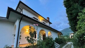 A two-story house with a white exterior, arched windows, and a pathway leading to the entrance. - Villa 'Lori' with Mountain View, Wi-Fi and Air Conditioning (Fornaci di Barga)