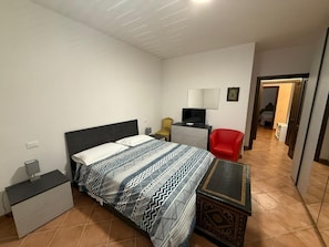 Ein Schlafzimmer mit einem Bett, einem Nachttisch, einem Sessel und einem Schreibtisch mit Stuhl.