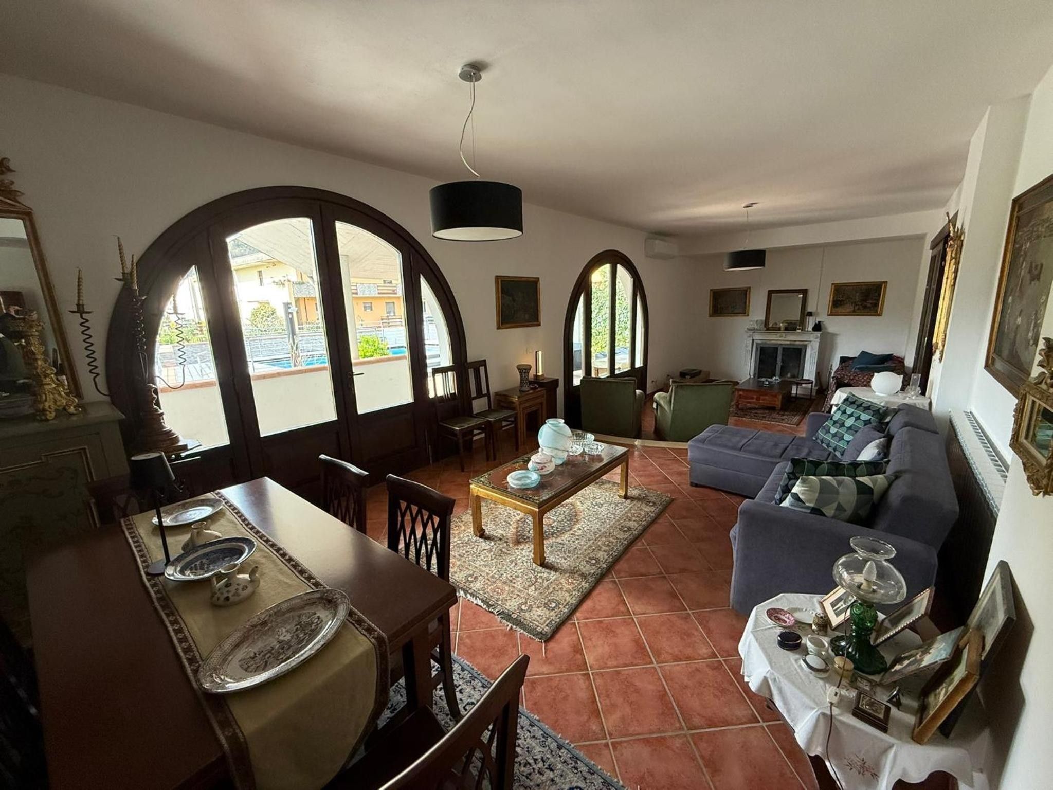 A living room with a dining area, large arched windows, a fireplace, and a sofa.