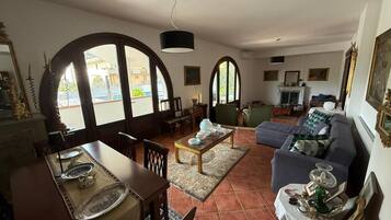 A living room with a dining area, large arched windows, a fireplace, and a sofa.