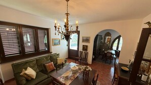 A dining area with a table set for four, a green sofa, and a chandelier. - Villa 'Lori' with Mountain View, Wi-Fi and Air Conditioning (Fornaci di Barga)