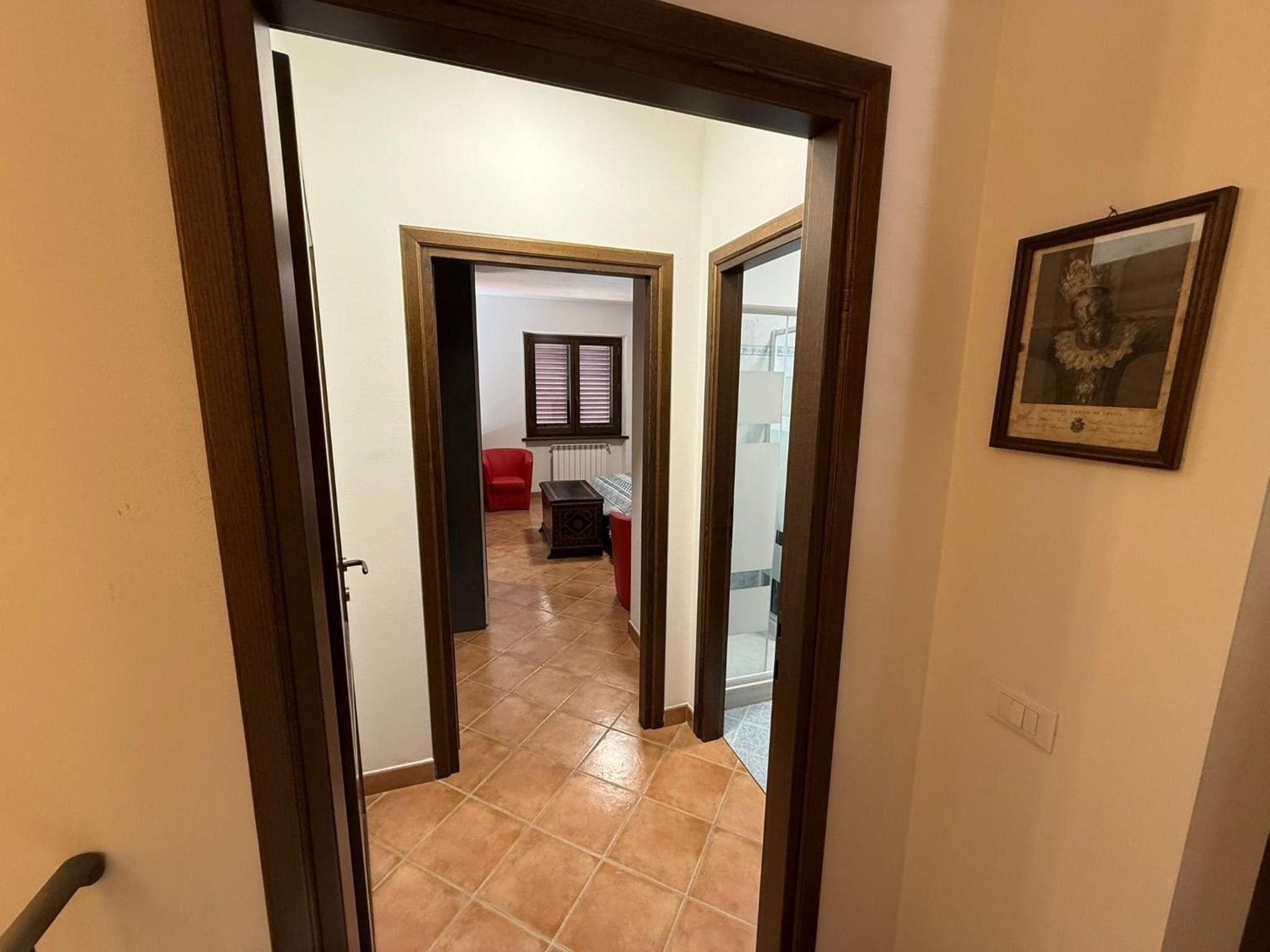 Ein Flur mit Fliesenboden, der in einen Wohnbereich mit einem roten Sofa und einem Fenster mit Jalousien führt.