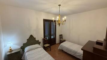 Quarto com duas camas de solteiro, mesa de cabeceira com abajur, cadeira de madeira e cômoda.