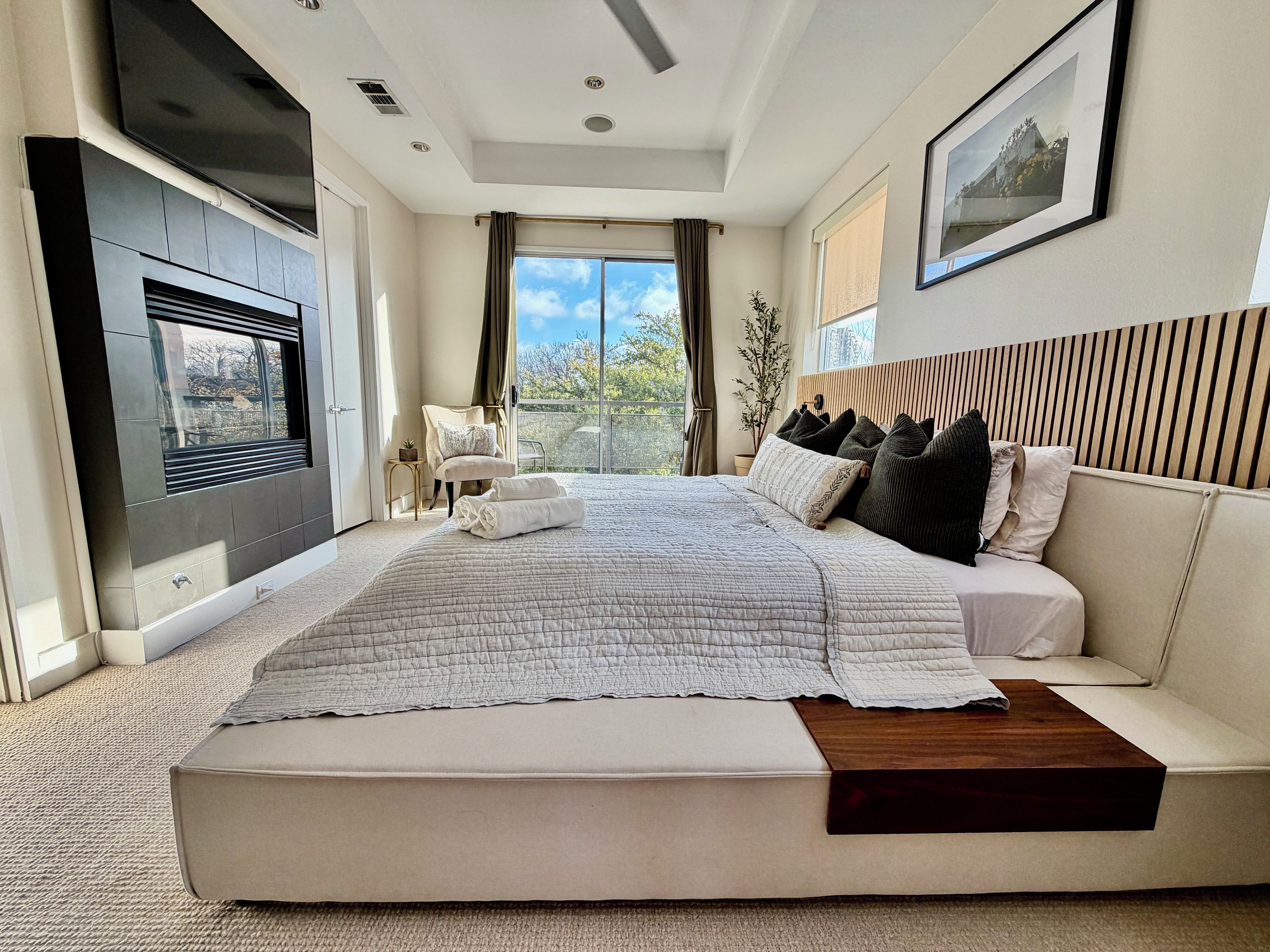 A modern bedroom with a large bed, a sofa, a TV, and a balcony with a view.