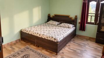 A bedroom with a wooden bed, a patterned bedspread, a wooden floor, and a window with curtains.