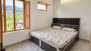 A bedroom with a bed, a window with a view of greenery, and a wall-mounted light fixture.