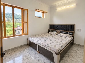 A bedroom with a bed, a window with a view of greenery, and a wall-mounted light fixture. - 2-bedroom house with Free Bus Stand Pick-Up & Drop-Off (Chamba)