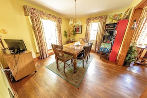 A dining area with a wooden table and chairs, a rug, and a bookshelf with various items. - Charming Shepherdstown Home - Walk to Downtown (Shepherdstown)