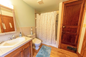 A bathroom with a wooden vanity, a toilet, a shower curtain, and a wooden door. - Charming Shepherdstown Home - Walk to Downtown (Shepherdstown)