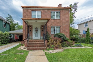 A two-story brick house with a front porch, a small garden, and a visible mailbox.