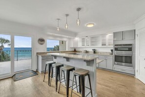 A modern kitchen with a large island, bar stools, and a view of the ocean. - Beach Funatics (Miramar Beach)