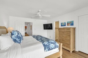 A bedroom with a bed, a ceiling fan, a TV, a wooden dresser, and a door. - Beach Funatics (Miramar Beach)