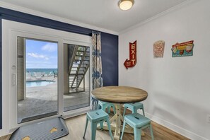 A room with a wooden table and two stools, a pool view, and an exit sign. - Beach Funatics (Miramar Beach)