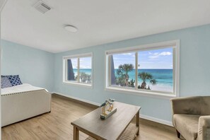 A room with a bed, a table, and two windows with a beach view. - Beach Funatics (Miramar Beach)
