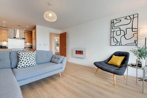 Ein modernes Wohnzimmer mit einem grauen Sofa, einem schwarzen Sessel und einem Wandbild im abstrakten Stil.