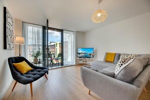 Ein modernes Wohnzimmer mit einer Couch, einem Sessel, einem Fernseher und einem großen Fenster.