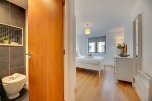 Ein modernes Badezimmer mit Toilette, einer Holztür und einem Duschbereich.