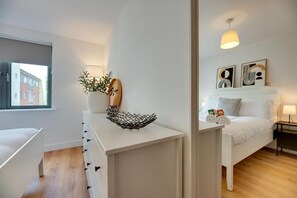 A modern bedroom with a white bed, a bedside table with a lamp, and artwork on the wall. - Stephenson View (Gateshead)