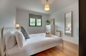 A modern bedroom with a single bed, a dresser, a mirror, and a window with a view of greenery. - Stephenson View (Gateshead)