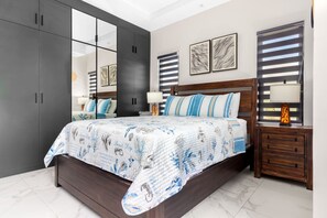 A bedroom with a large bed, dark wooden wardrobe, and a nightstand with a lamp. - Sea La Vie | Pool |2BR | Gated | Walk to the Beach (Llandovery)