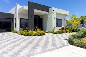 A modern building with a flat roof, a covered entrance, and a paved driveway. - Sea La Vie | Pool |2BR | Gated | Walk to the Beach (Llandovery)