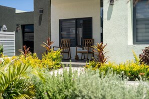 A modern building with a patio area featuring two wooden rocking chairs and a small table. - Sea La Vie | Pool |2BR | Gated | Walk to the Beach (Llandovery)
