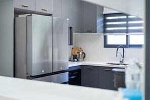 A modern kitchen with a stainless steel refrigerator, a dishwasher, and a window with blinds. - Sea La Vie | Pool |2BR | Gated | Walk to the Beach (Llandovery)