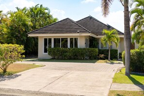 A two-story house with a covered driveway, surrounded by lush greenery and palm trees. - Richmond Retreat | Pool| Gym | Gated| Beach Access (Plantation Village)