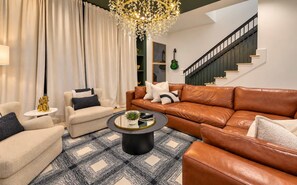 Ein modernes Wohnzimmer mit einem braunen Ledersofa, einem runden Couchtisch und einer Kronleuchter.