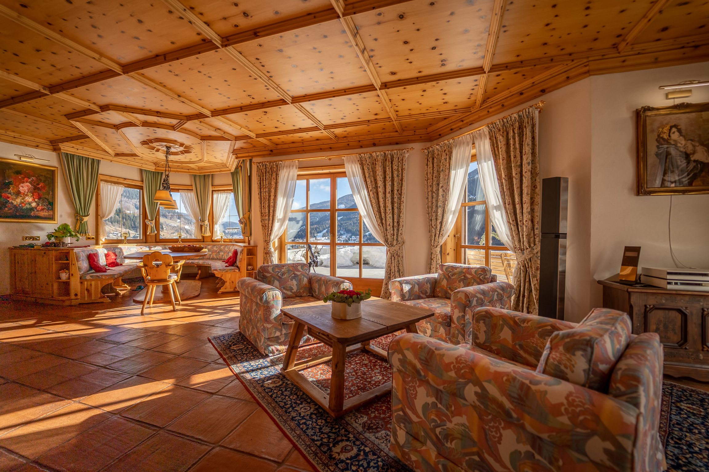 A cozy living room with a wooden ceiling, large windows, and a view of the mountains.