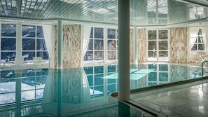 Una amplia piscina cubierta con vistas despejadas a montañas nevadas a través de grandes ventanales.