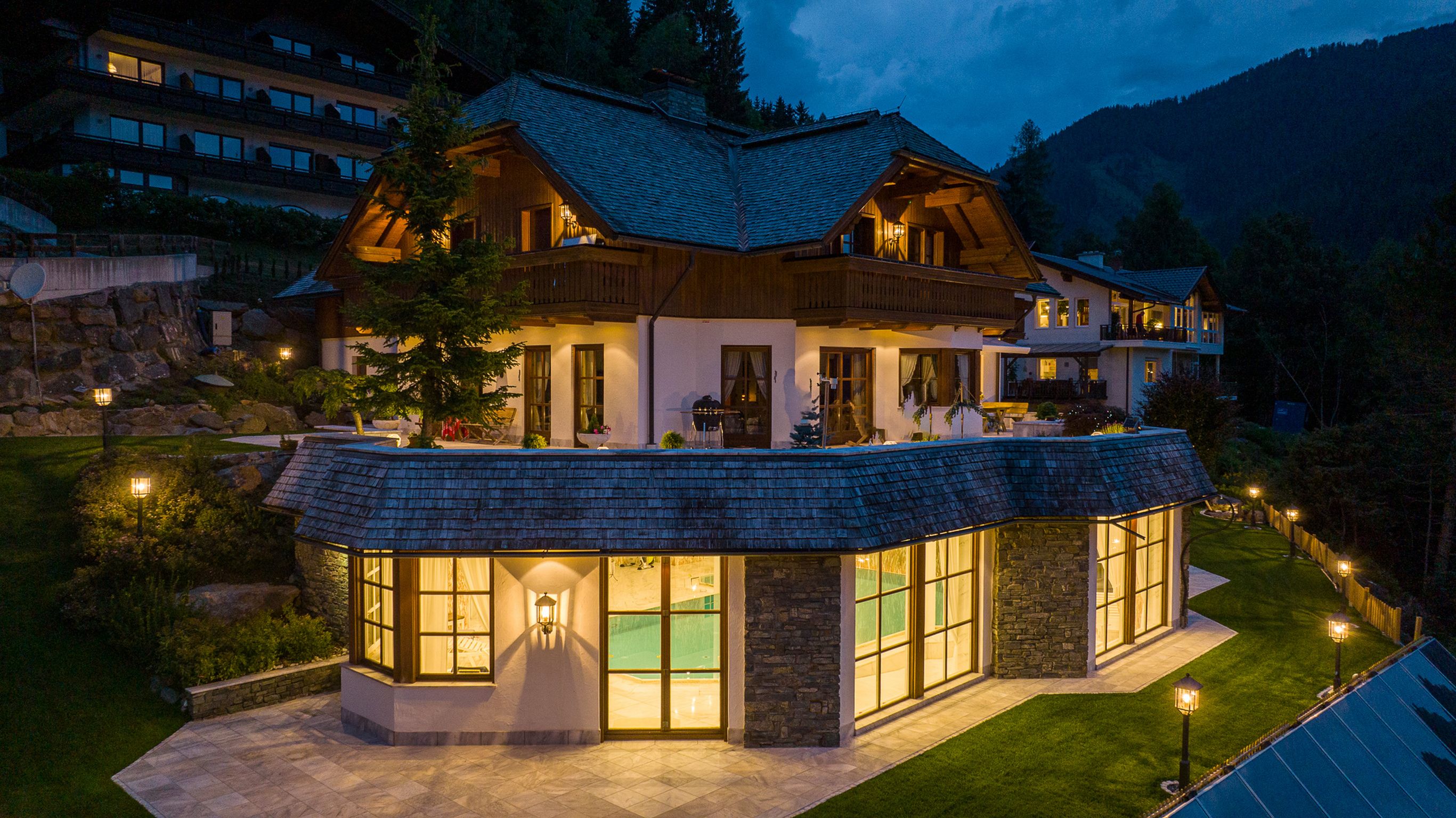 A large, multi-story house with a prominent balcony and a separate glass-enclosed structure with a stone facade.