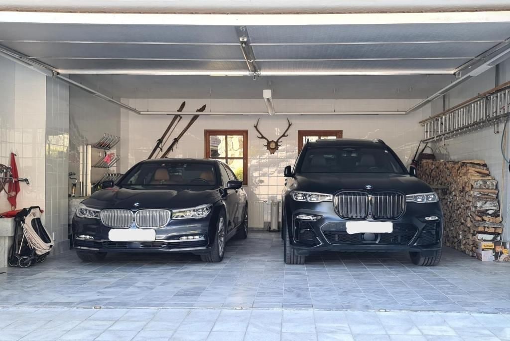 Uma garagem com dois carros estacionados lado a lado, um suporte para esquis e um chifre de veado fixado na parede.