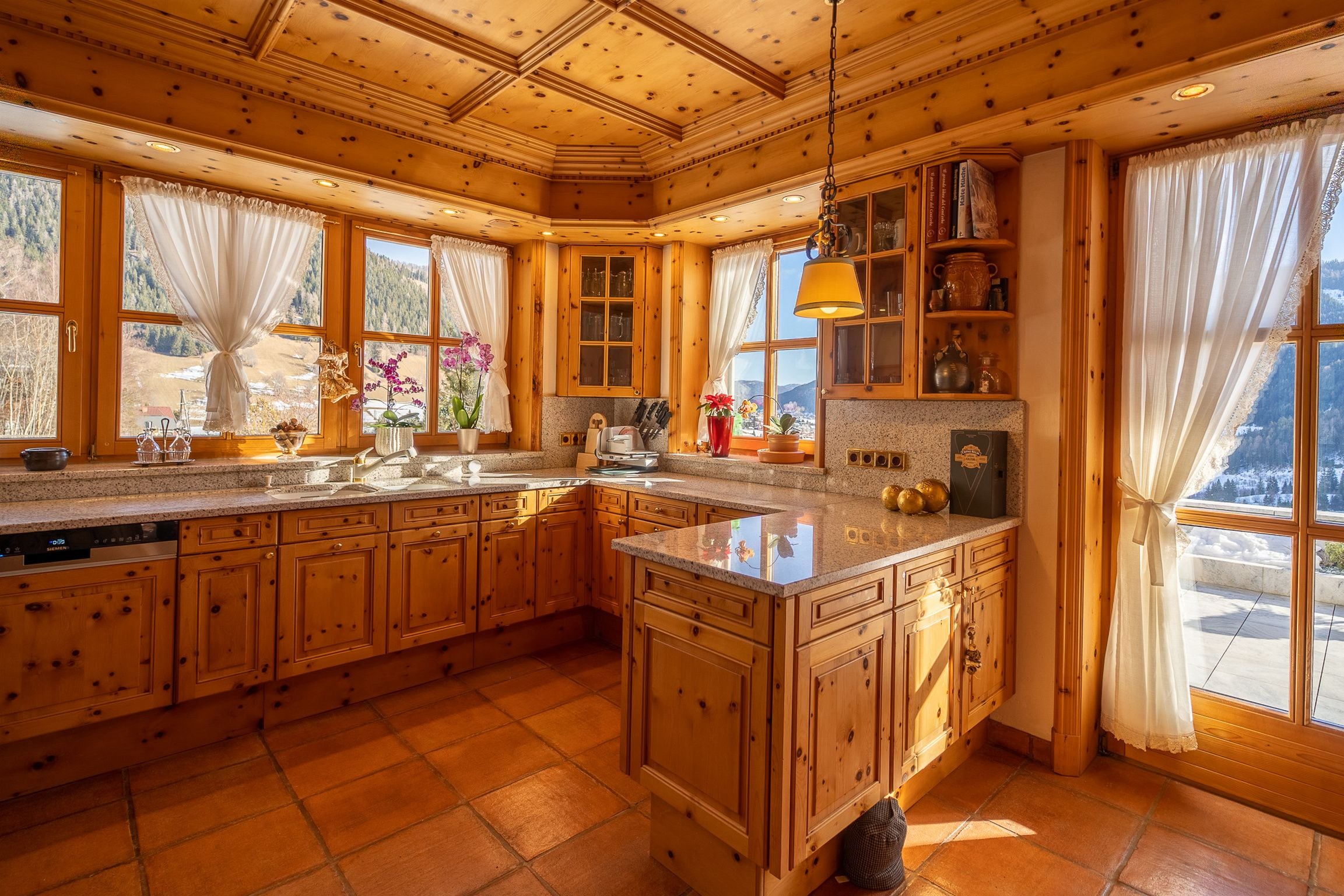 A spacious kitchen with wooden cabinets, granite countertops, and large windows offering scenic views.