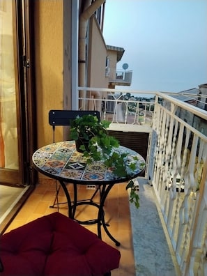 Un balcón con una mesa, una silla, una planta en maceta y un cojín rojo.