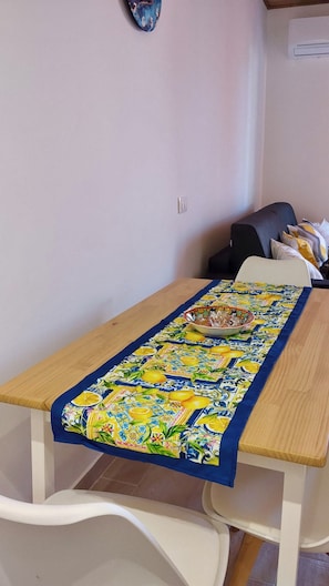 Una habitación con una mesa de madera, un mantel estampado, una silla blanca y un sofá oscuro con cojines.