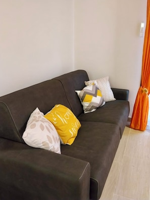 En mørkebrun sofa med tre puder, hvoraf den ene har pote-mønster, den næste gul og grå gulmønster, og den sidste tekst i hvid.