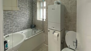 Et badeværelse med badekar, vask, toilet og et spejl.
