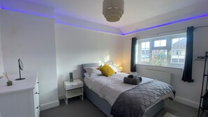 Et soveværelse med seng, sengebord, lampe og et vindue med gardiner.