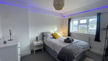 Ein Schlafzimmer mit Bett, Nachttisch, Lampe und einem Fenster mit Vorhängen.