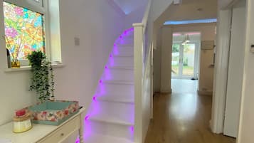 Eine Treppe mit violetter Beleuchtung, eine weiße Wand, ein Fenster mit farbigem Glasdekor und ein Holzboden.