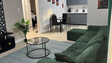 A modern living room with a green sofa, a glass coffee table, and a patterned rug.