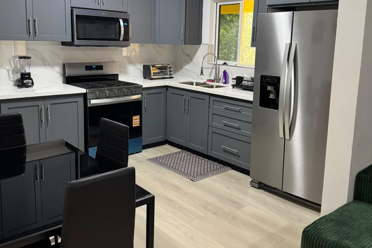 A modern kitchen with grey cabinets, a stainless steel refrigerator, a microwave, and a stove.