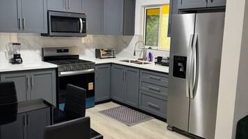 A modern kitchen with grey cabinets, a stainless steel refrigerator, a microwave, and a stove.