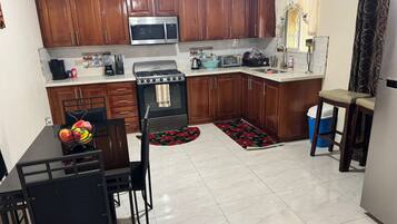 Una cocina compacta con armarios de madera, un microondas de acero inoxidable, una estufa a gas y un comedor con una mesa y sillas negras.