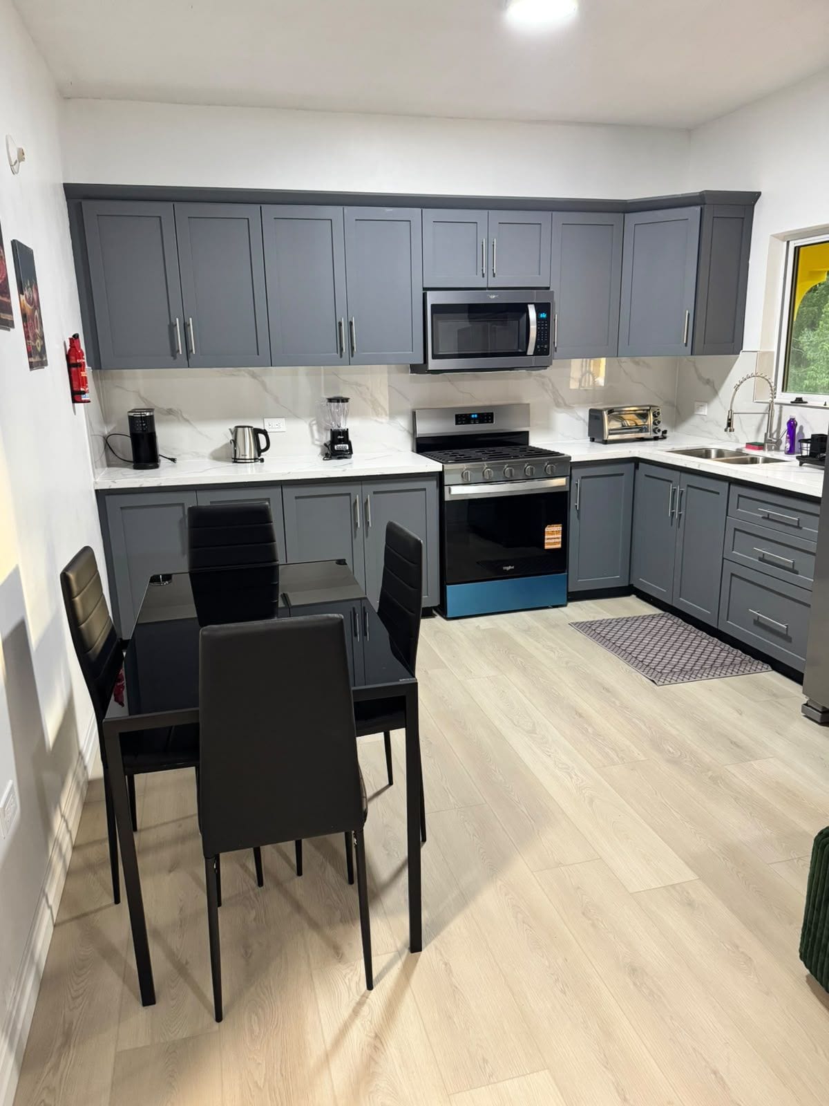 A compact kitchen with grey cabinets, a microwave, a toaster, and a dining table with chairs.