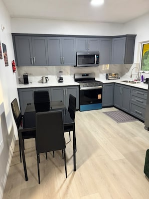 A compact kitchen with grey cabinets, a microwave, a toaster, and a dining table with chairs.