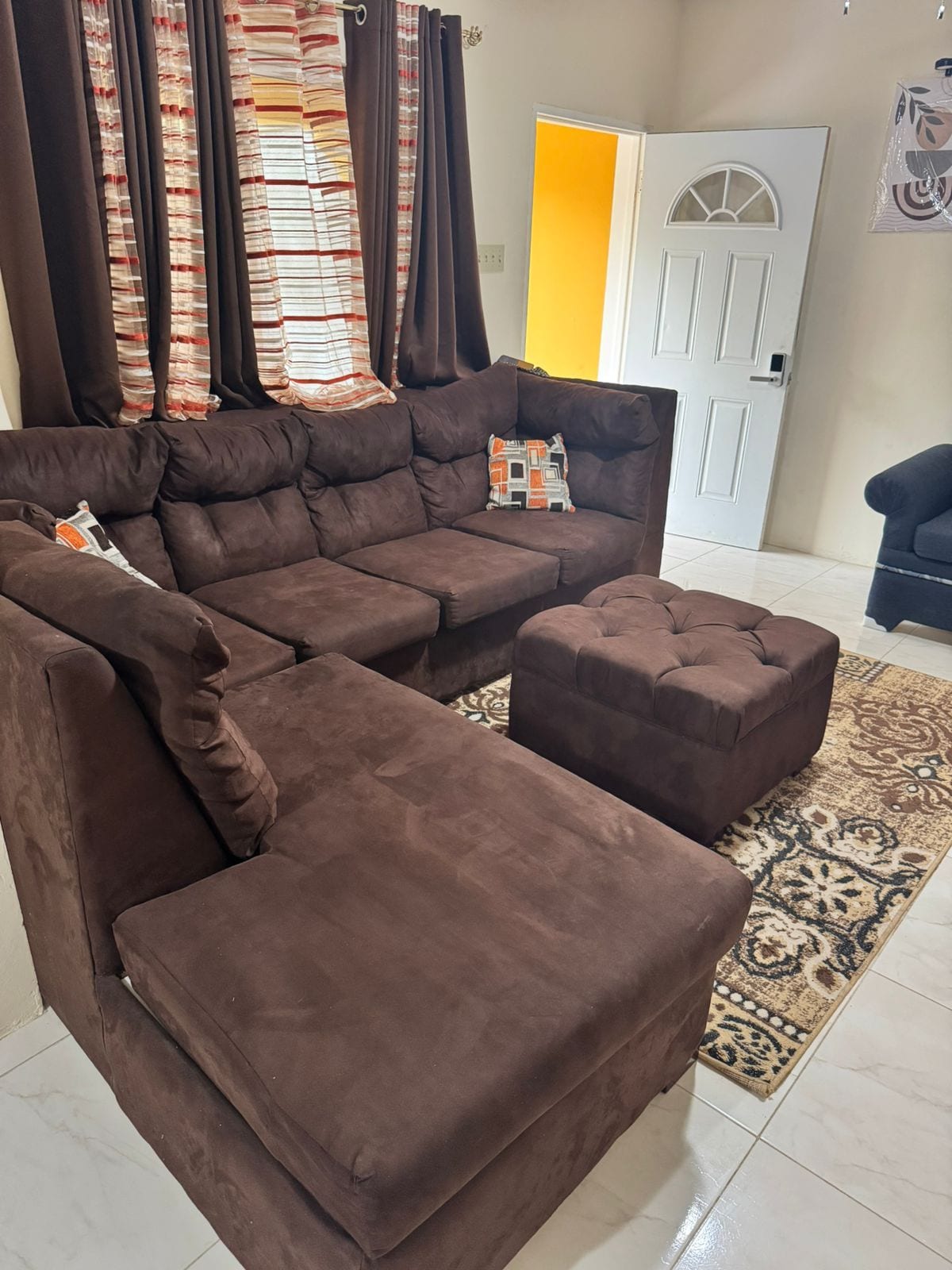 A brown sectional sofa with a matching ottoman, a patterned rug, and a door with a window in the background.